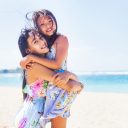 Couple of lovely asian sisters hugging on a beach (looking at camera)